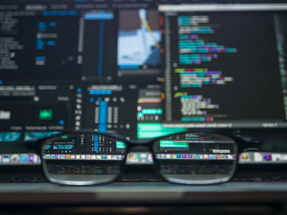 A close-up of eyeglasses with data codes reflected on the lenses, symbolizing the role of data security and technology in modern cybersecurity.