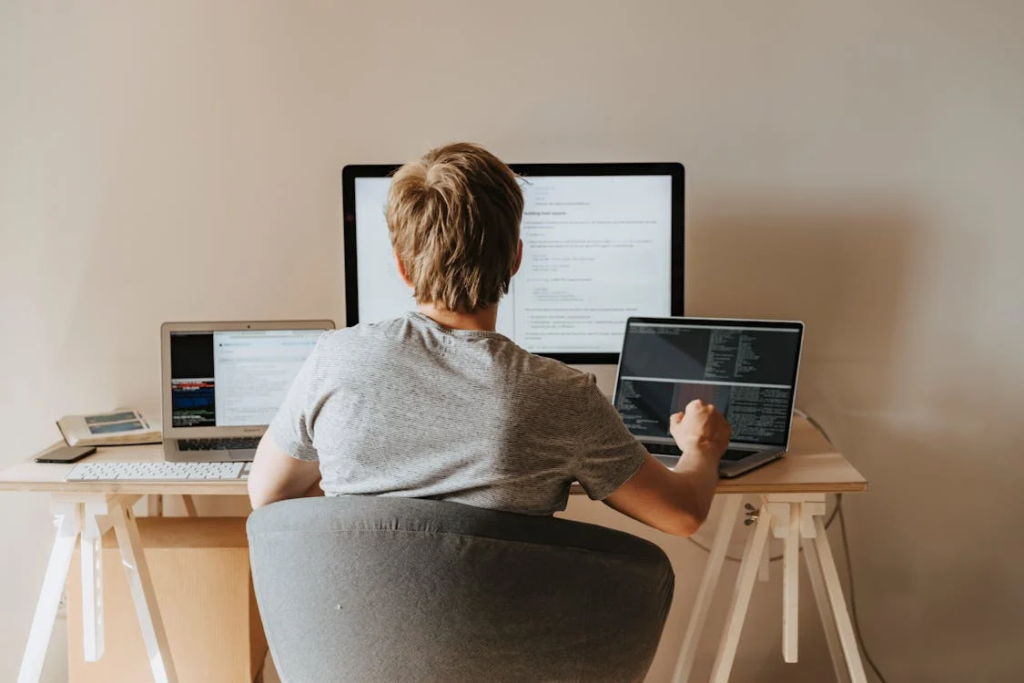A boy sitting on a grey chair, using a laptop computer, representing the use of AI and technology for small businesses.